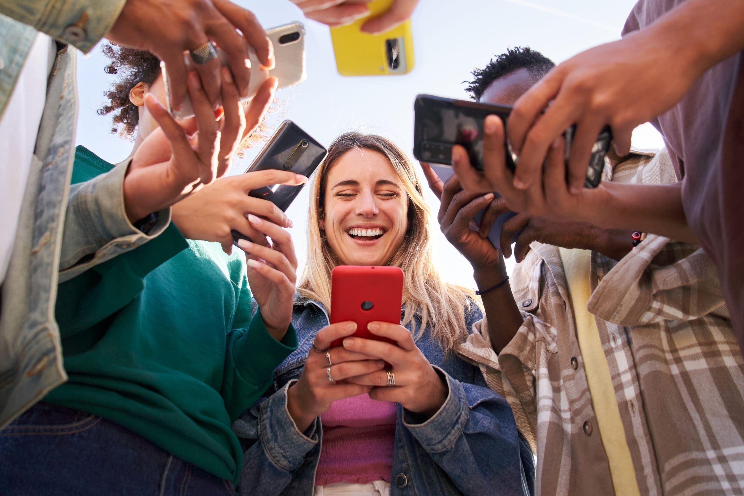 A group of people standing close together, smiling, and looking at their smartphones.